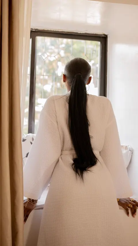 Mulher de roupão olhando pela janela depois do banho (foto ilustrativa)